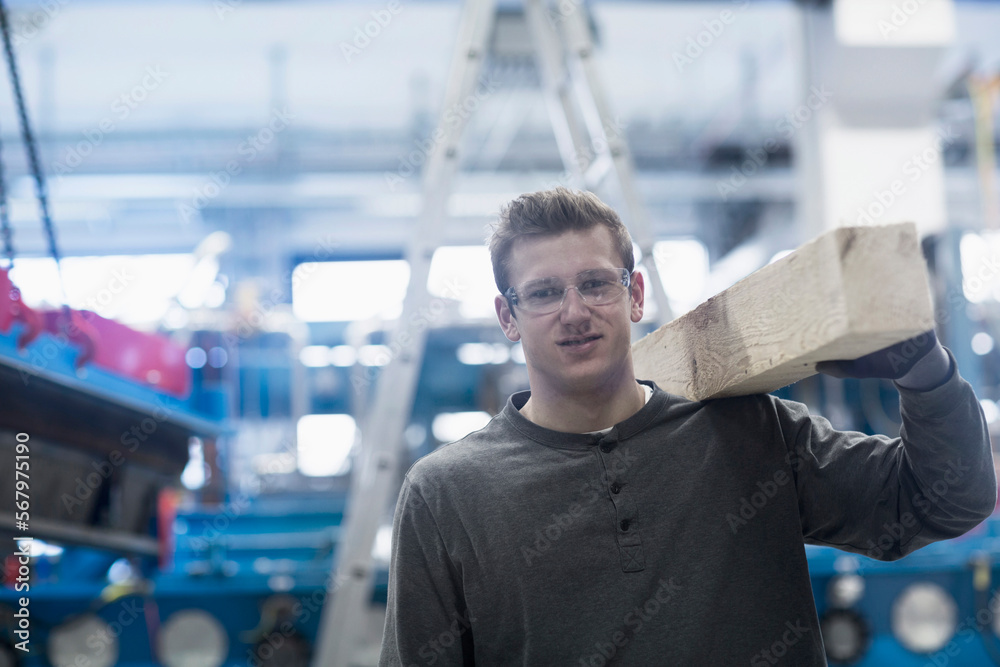 Young male engineer carrying wood on his shoulder in an industrial plant, Freiburg Im Breisgau, Baden-Württemberg, Germany Young male engineer carrying wood on his shoulder in an industrial plant, Freiburg Im Breisgau, Baden-Württemberg, Germany