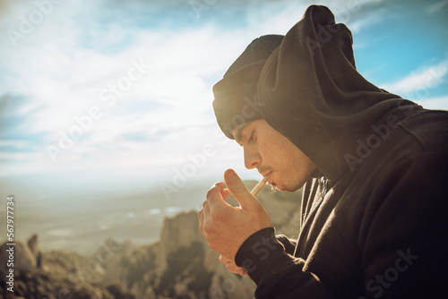 Boy smoking a marijuana joint on top of a mountain during sunset