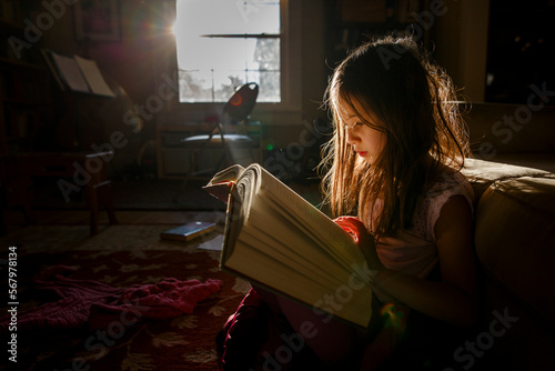 A small child sits in patch of bright sunlight reading a large book