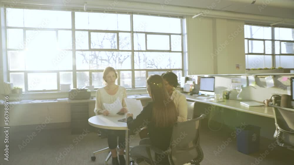 Handheld shot of businesswomen reading documents while working at desk in office