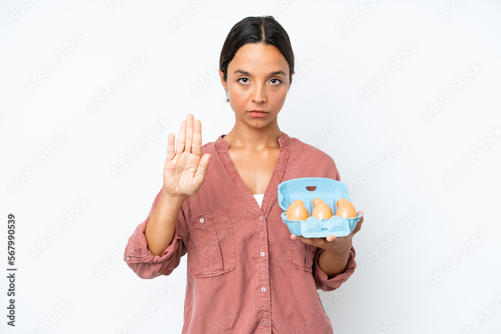 Young hispanic woman holding eggs isolated on white background making stop gesture Young hispanic woman holding eggs isolated on white background making stop gesture