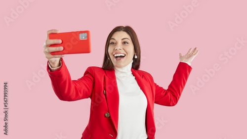 Overjoyed young woman isolated on pink studio background talk on video call on smartphone. Smiling girl blogger or influencer have webcam live broadcast on cellphone. Online communication.