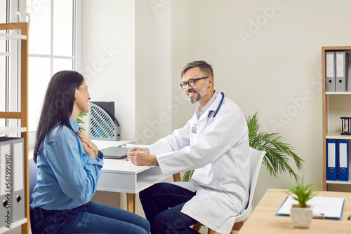 Male doctor consulting female patient in medical clinic. Positive professional physician talking to smiling young woman at medical check up visit. Healthcare and medical treatment concept
