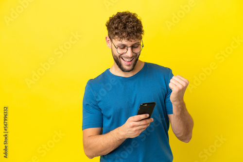 Young handsome caucasian man isolated on yellow background with phone in victory position