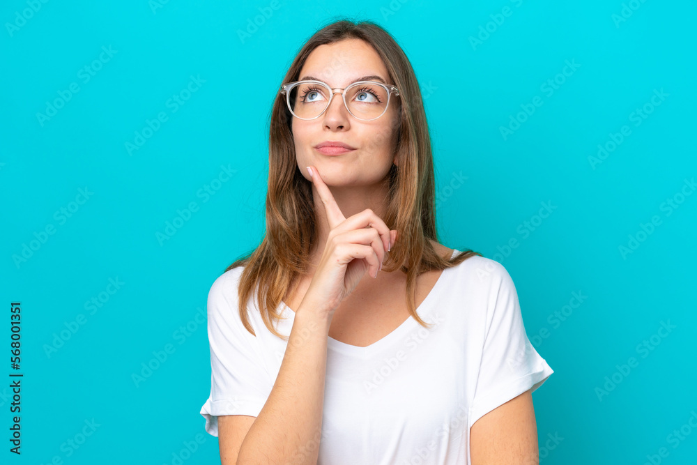 Young caucasian woman isolated on blue background With glasses and looking up Young caucasian woman isolated on blue background With glasses and looking up