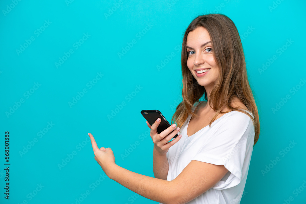 Young caucasian woman isolated on blue background using mobile phone and pointing back Young caucasian woman isolated on blue background using mobile phone and pointing back
