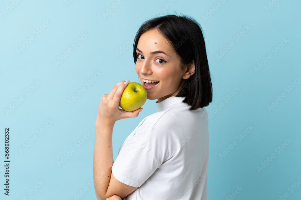 Young caucasian woman isolated on blue background eating an apple Young caucasian woman isolated on blue background eating an apple
