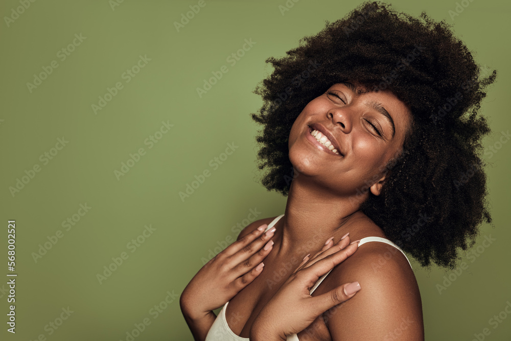 Delighted young black lady smiling with closed eyes against green background Delighted young black lady smiling with closed eyes against green background