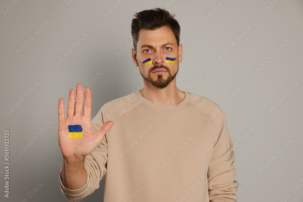 Angry man with drawings of Ukrainian flag against light grey background, focus on palm Angry man with drawings of Ukrainian flag against light grey background, focus on palm