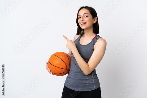 Young woman playing basketball isolated on white background pointing finger to the side