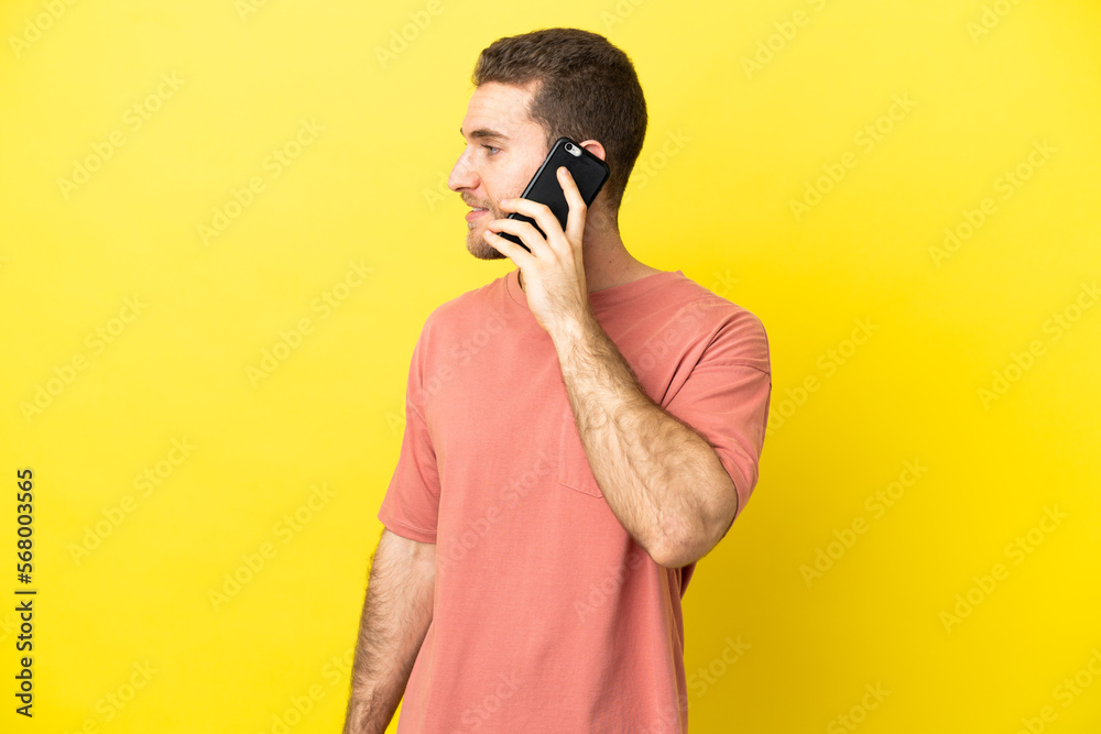 Handsome blonde man using mobile phone over isolated background looking side Handsome blonde man using mobile phone over isolated background looking side