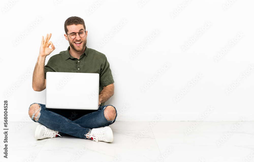 Young man sitting on the floor showing ok sign with fingers Young man sitting on the floor showing ok sign with fingers