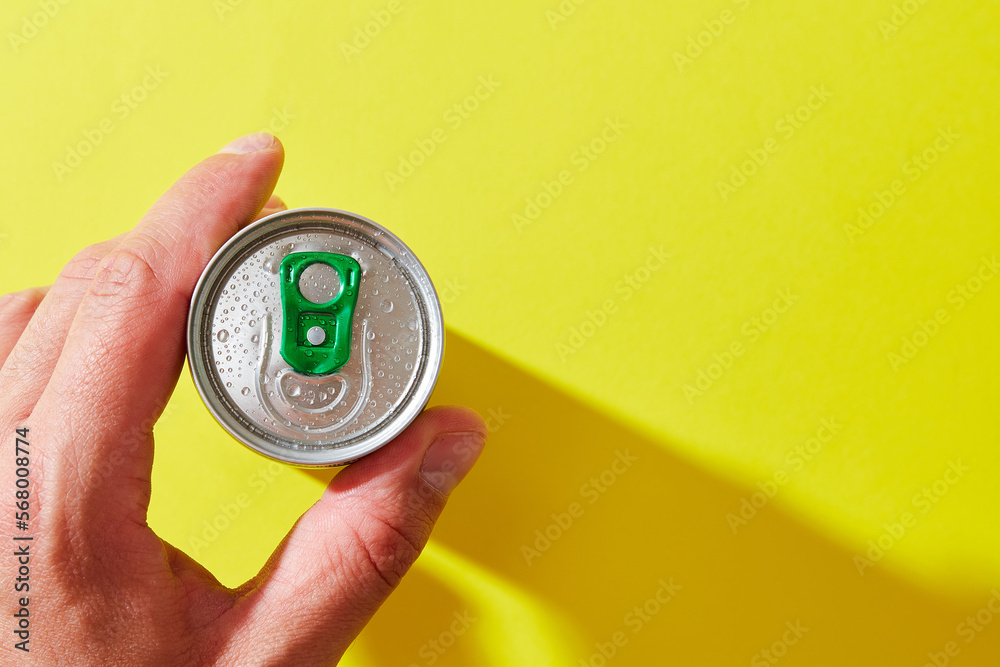caucasian man hand hold can with green pull tab, water drops, condensate on yellow background with hard light shadow, top view caucasian man hand hold can with green pull tab, water drops, condensate on yellow background with hard light shadow, top view