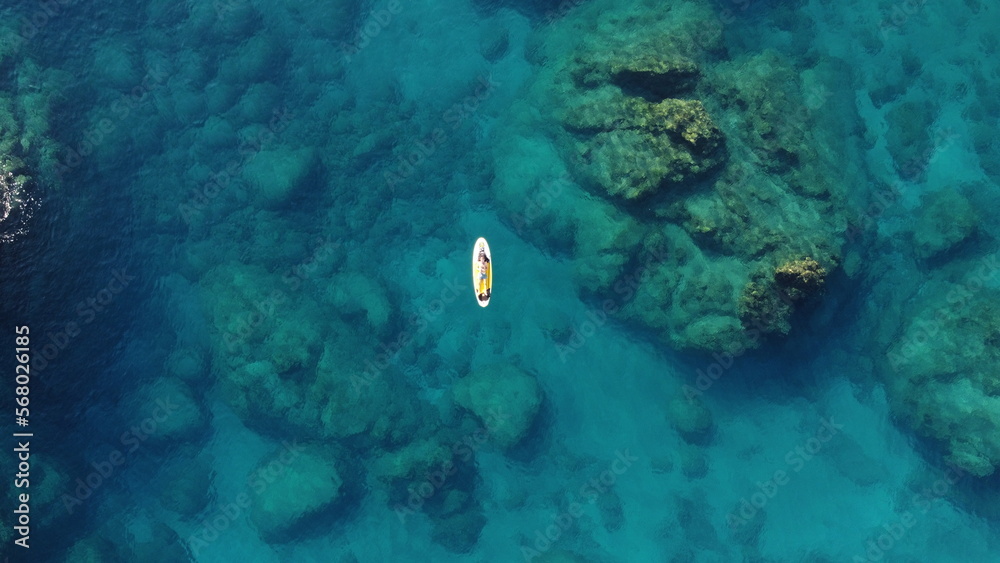 Fototapeta premium A man lies on a Supboard in the Mediterranean sea with stones at the bottom of the sea from a drone