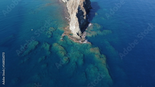 A rock in the mediterranean sea with large stones at the bottom from a drone