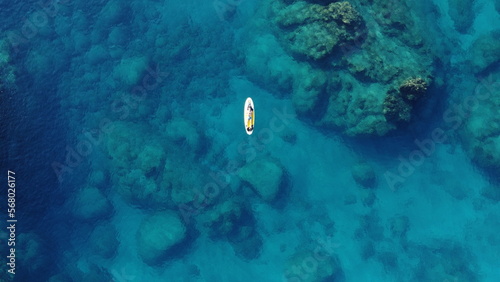 A man lies on a Supboard in the Mediterranean sea with stones at the bottom of the sea from a drone