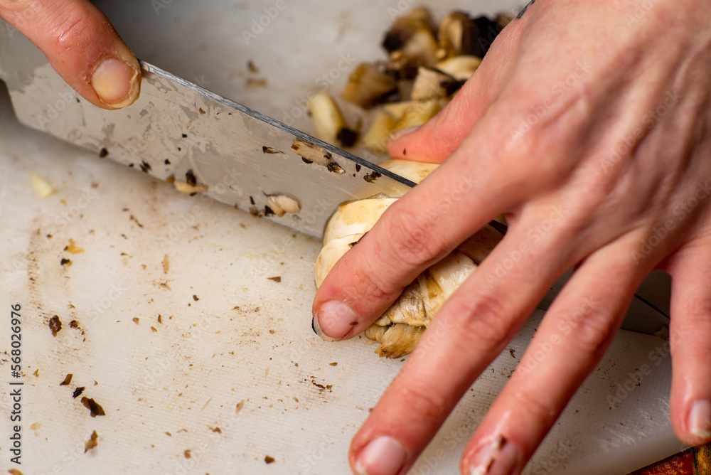 Sliced champignon mushrooms on a cutting board. Women's hands cut mushrooms with a knife.