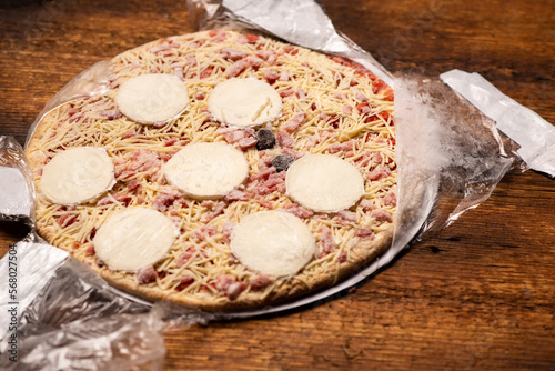 Frozen pizza in an open package on a wooden background. Semifinished. Preparing to cook fast food.