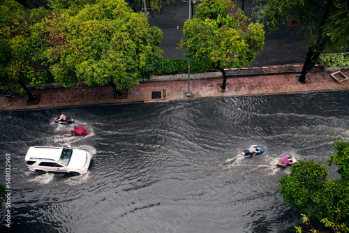 Street flood after a heavy rain in an Asian city. Car and motorbikes driving in deep water on a flooded road