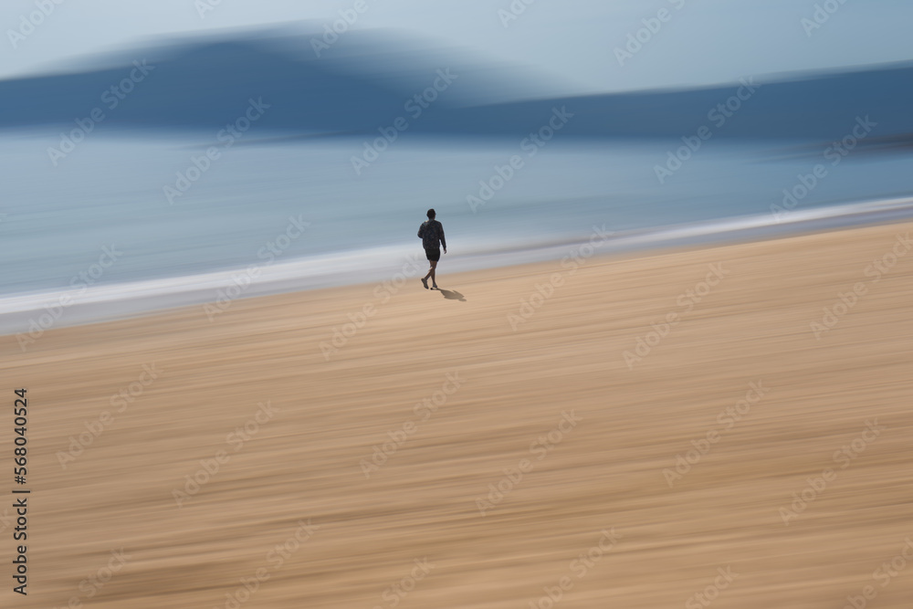 Lonely walk.  A man walks along a beach.  A path blur abstract edit has been applied to the background.