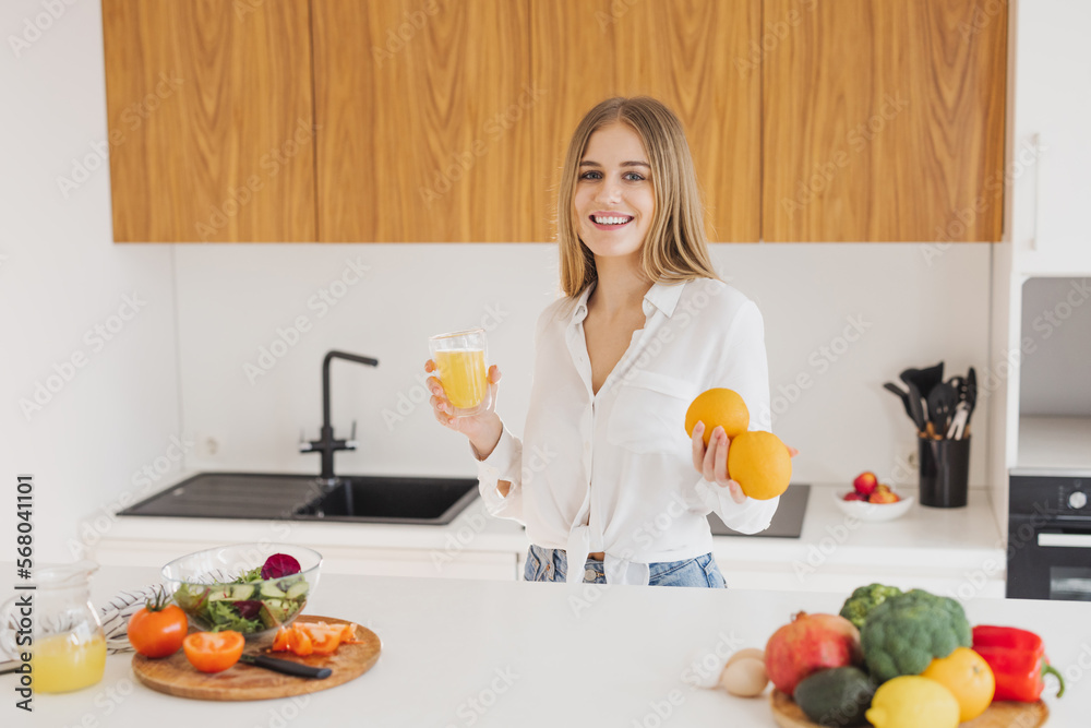 A happy blonde woman is drinking juice in the kitchen A happy blonde woman is drinking juice in the kitchen
