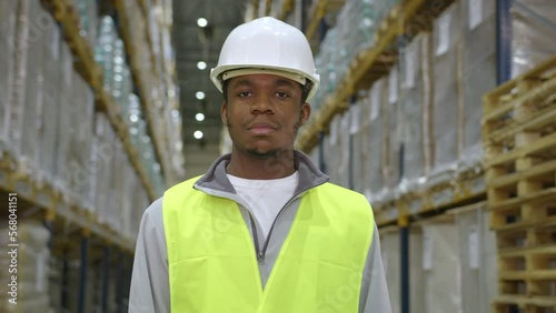 African American picker in hardhat against racks with storing goods in warehouse photo
