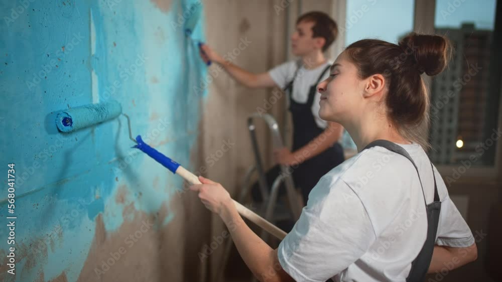 Painters, guy and girl paint walls in room with roller. Wall