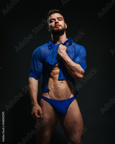 Fotografie, Obraz Sexy muscled male model in blue shirt and blue swimwear on black background