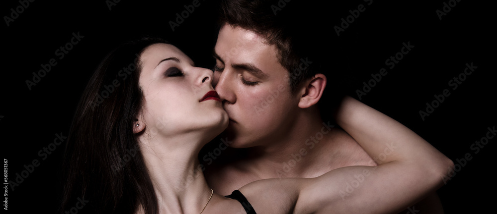 Beautiful young couple hugging and kissing as part of the sexual foreplay isolated on the black background