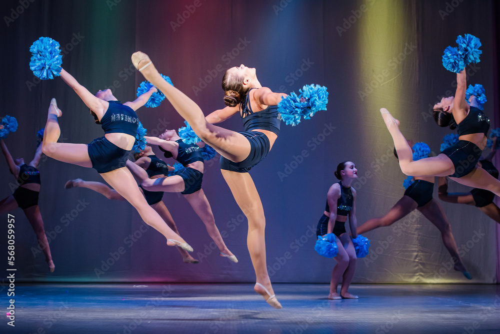 athletes perform on stage, young cheerleaders perform at the cheerleading championship, girls in a jump, girls are holding pompons, hands raised up, girls dancer practicing mixed dance and stretching