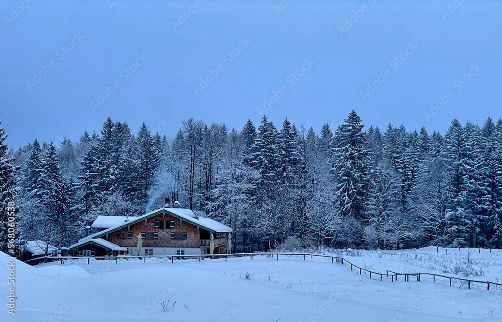 Berghütte (Frasdorfer Hütte) an einem trüben Winterabend in verschneiter Landschaft am Waldrand im Hochries Gebiet, Alpen, Chiemgau, Bayern, Deutschland