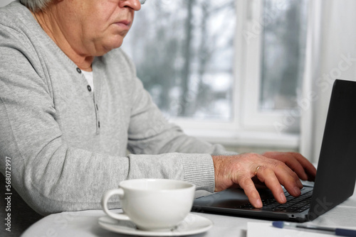 Senior male business owner in glasses sitting at desk in front of laptop. Successful older male working at home. Grey haired 60s - 70s Aged busy man typing keyboard looking at display. Distance office
