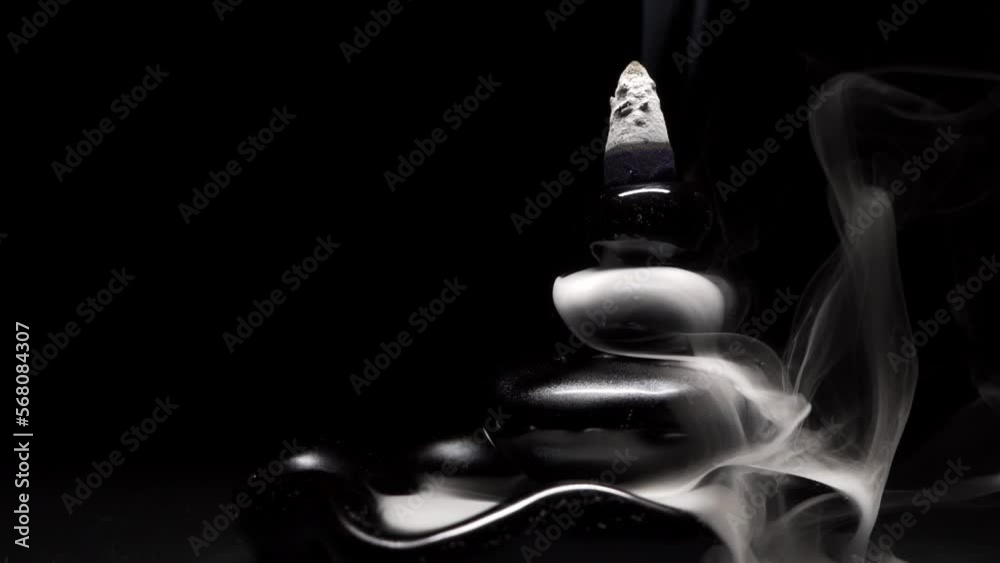 Thick white fragrant smoke, similar to liquid, flows down in smooth streams and waves from a cone of incense burning on a black porcelain stand for aromatherapy, relaxation, meditation or yoga
