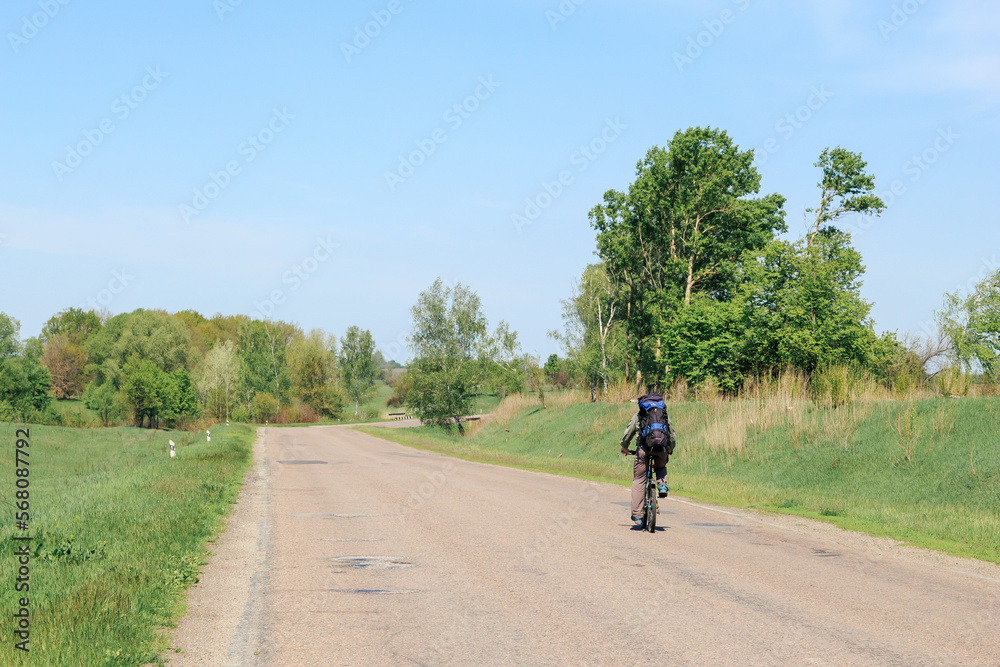 A lone cyclist with a backpack rides a mountain bike on a sunny summer day on a highway cycling route. Travel photo, summer activity