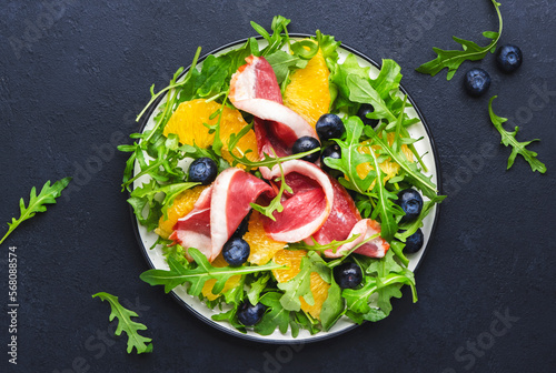 Delicious salad with smoked duck, oranges, blueberries, arugula and lettuce, black table background, top view