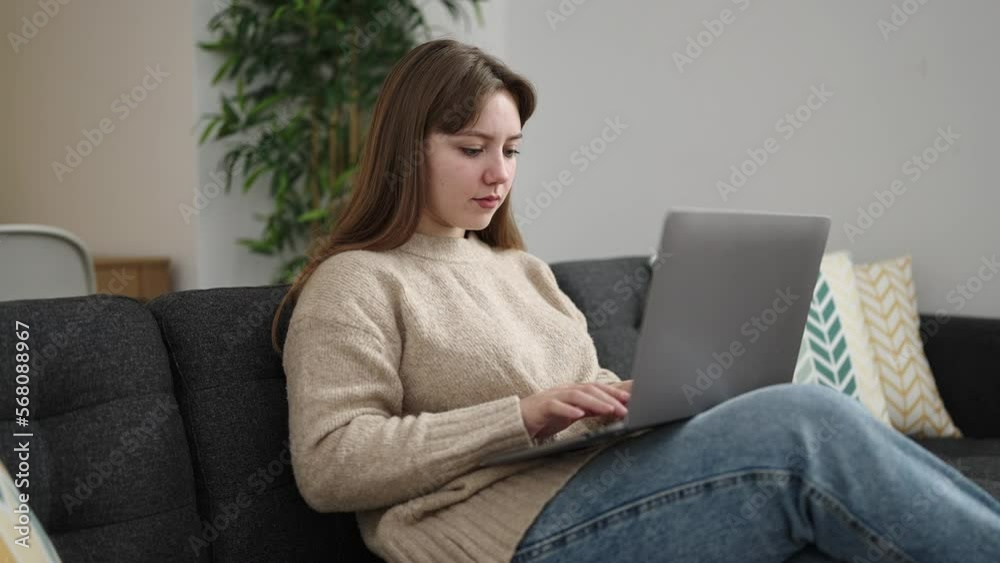 Young blonde woman using laptop sitting on sofa at home Young blonde woman using laptop sitting on sofa at home