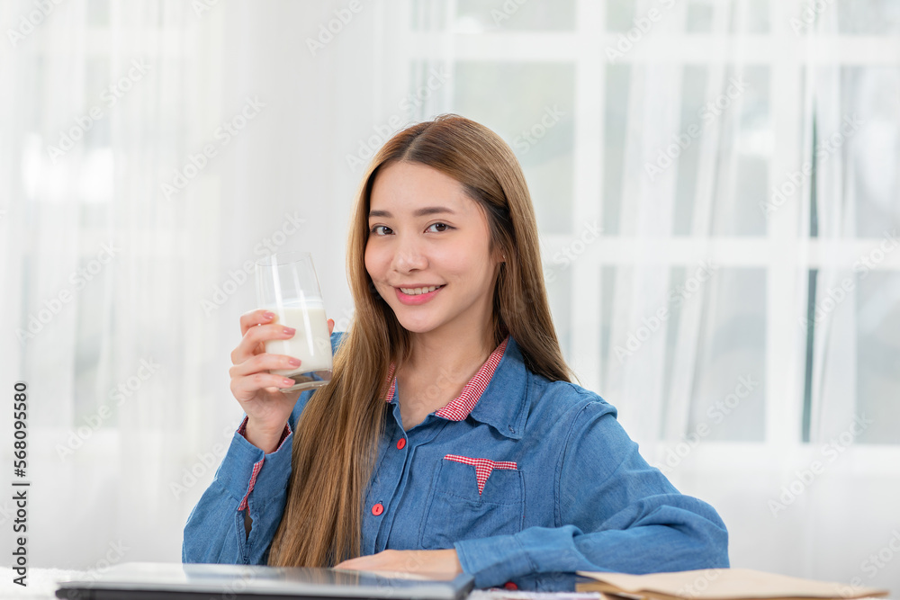 Healthy Young Asian woman Drinking milk with calcium for strong bone at home. Smiling indian woman holding soy milk on glass enjoy with nutrition wellness life.Wellness with natural milk fresh Concept