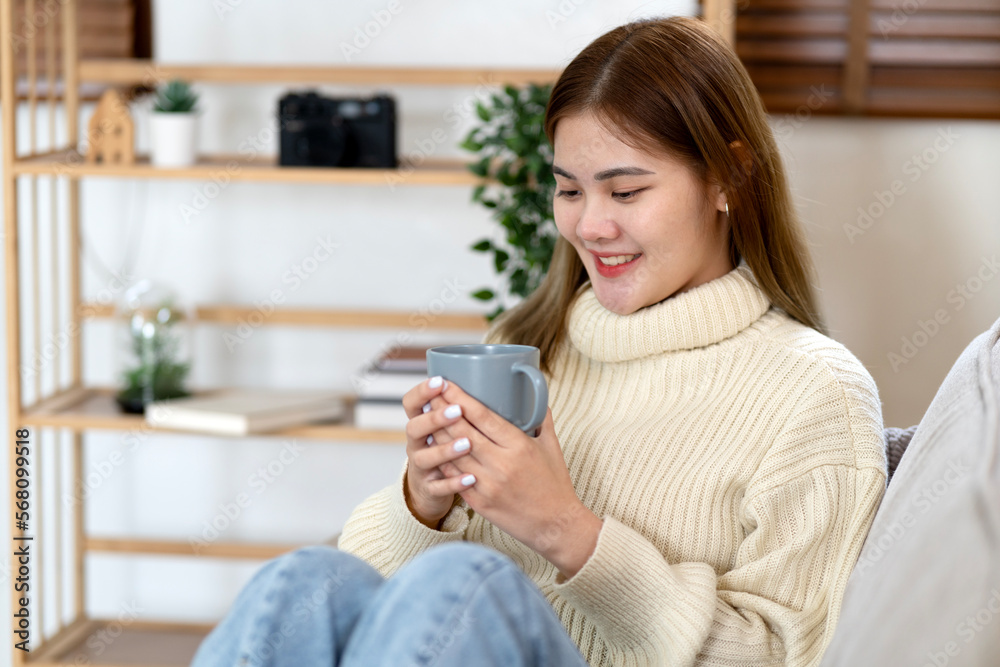 young asian woman holding a cup of coffee and a book on the cozy sofa young asian woman holding a cup of coffee and a book on the cozy sofa