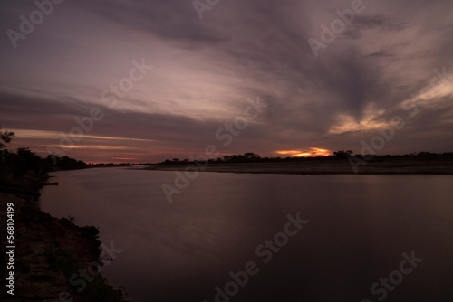 Long exposure shot of Corriente river in Esquina, Corrientes, Argentina, at sunset. Beautiful blurred water effect, dramatic clouds and hiding sun at nightfall. 