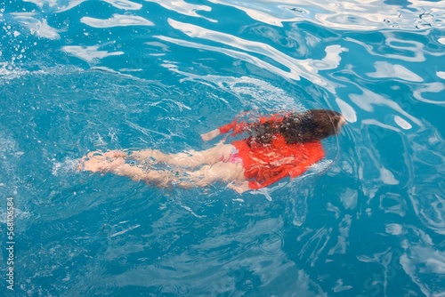 Child girl diving into the blue pool.
