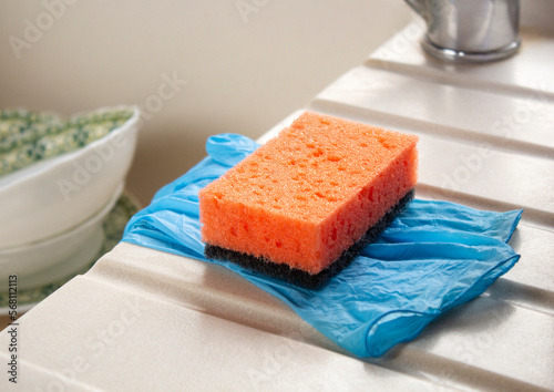 Close-up orange dishwashing sponge and gloves on the edge of kitchen sink