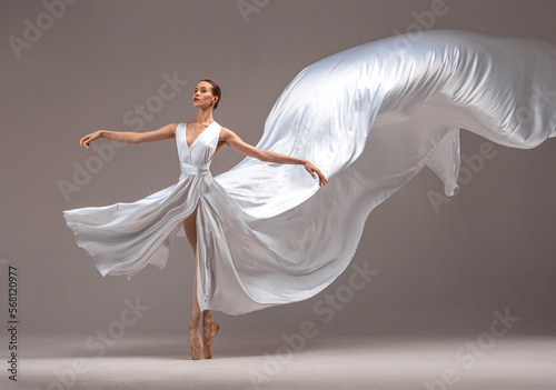 Fototapeta Naklejka Na Ścianę i Meble -  Ballerina in white ballet dress danсing on pointe shoes in white studio.