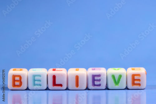 Square beads spelling the word believe against a graded blue background. Business motivation and inspiration with copy space above.