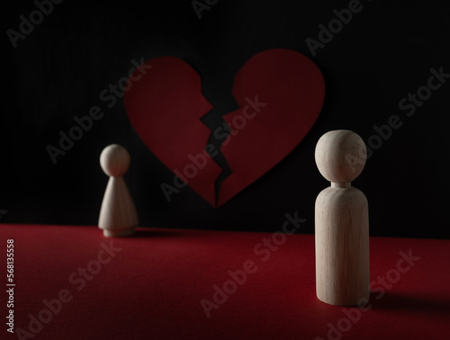 The wooden peg doll male standing away from the female with a broken red heart in black and red background. Marriage, relationship, break up, concept.