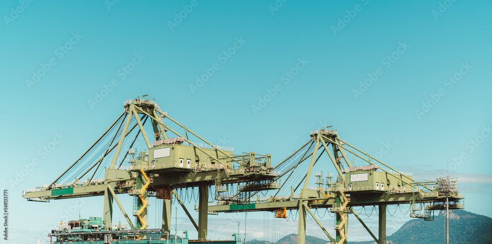 The capture of two massive yellow container handling cranes at work at the bustling dockside of Rio de Janeiro. These cranes stand tall, dominating the skyline as they expertly maneuver containers