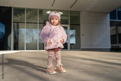 Small caucasian girl toddler stand in front of building in winter day