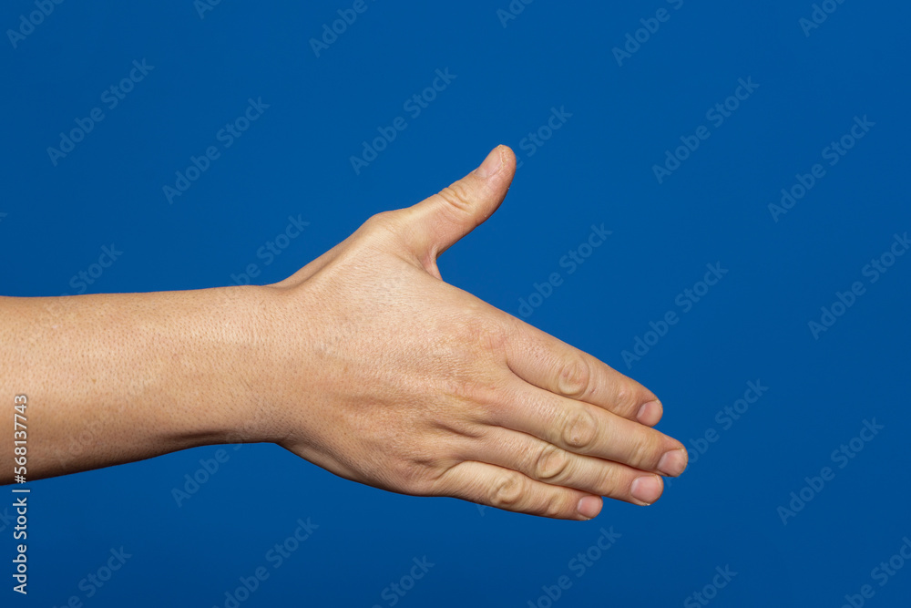 Man stretching out his hand to handshake isolated on a blue background. Man's hand ready for handshake. Man stretching out his hand to handshake isolated on a blue background. Man's hand ready for handshake.
