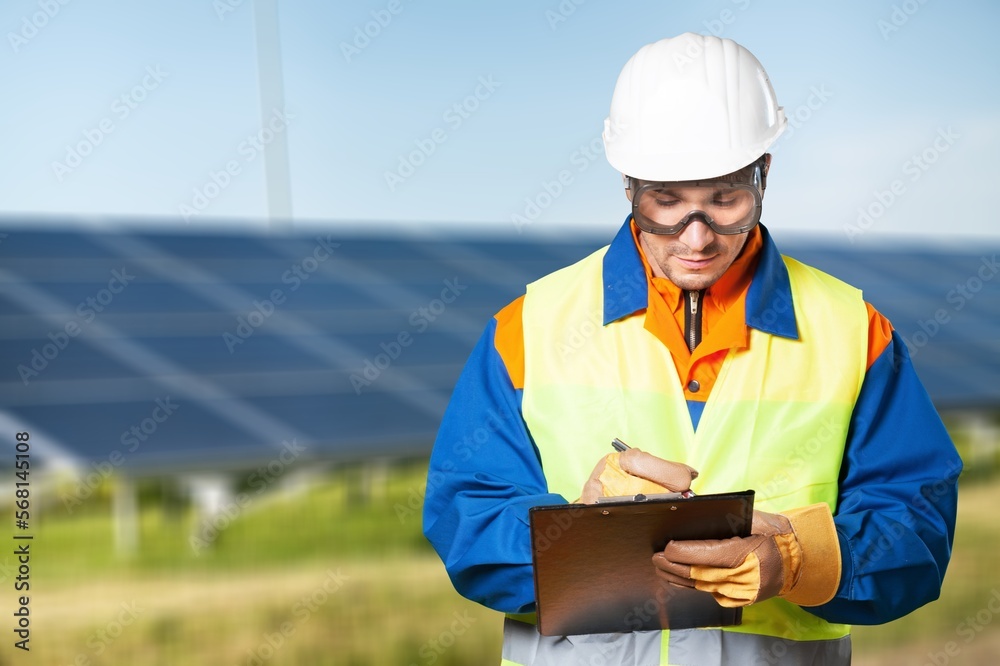Young engineer in helmet with clipboard at solar farm