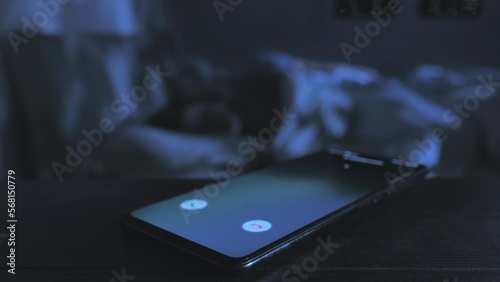infidelity love affair,close up on mobile phone receiving incoming call while a married couple sleep on bed in the background,betrays cheating concept