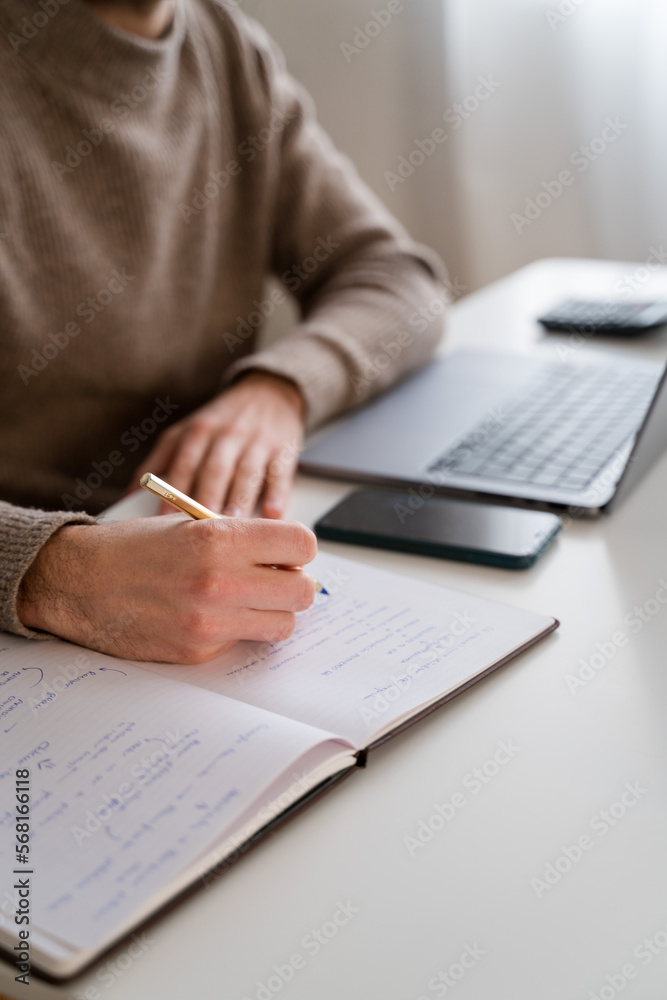 Crop man writing in notepad while working on project Crop man writing in notepad while working on project